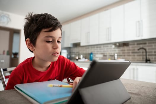Elementary school student boy on distance learning, doing homework, studying online, watching webinar on digital tablet