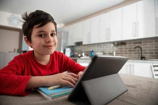 Elementary school student boy on distance learning, smiling looking at camera while watching webinar on digital tablet