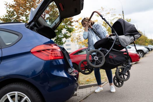 young mother driver puts a baby stroller into the luggage compartment of the car
