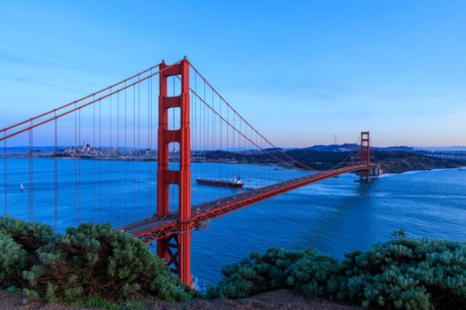 Cargo ship sails under iconic Golden Gate Bridge to San Francisco in blue hour