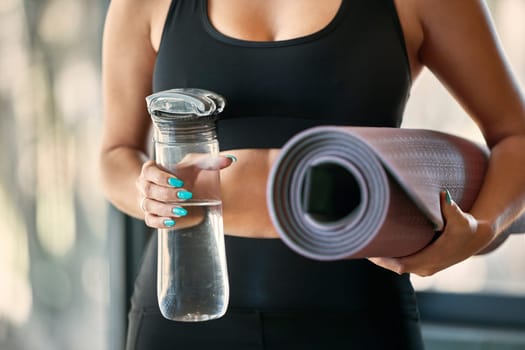 Yoga mat, hands and water bottle for fitness in gym, health or wellness workout. Pilates, training and hand of woman yogi with liquid for hydration and rug to start exercise, mediation or stretching.