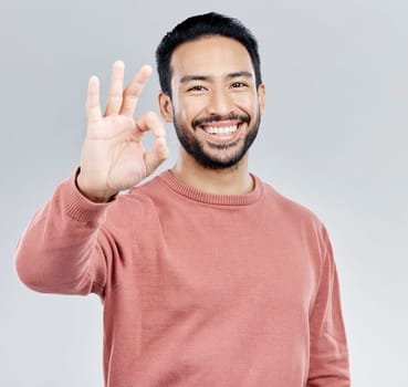 Hand, portrait and okay sign by man in studio with yes, vote or approval gesture against grey background. Finger, emoji and perfect symbol by asian male happy with decision, thank you or satisfied