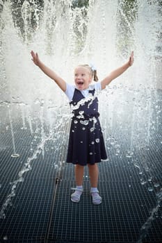 Little girl of elementary school student in modern school uniform outdoors near the fountain water jets. Female child schoolgirl having fun. Back to school in september 1 in Russia