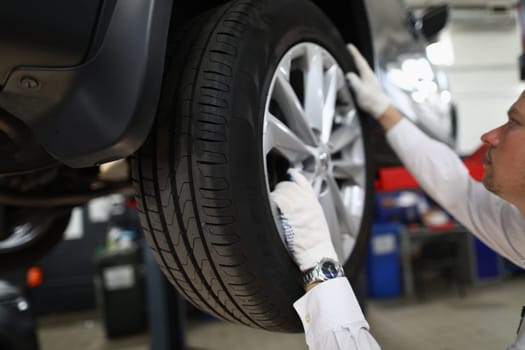 Auto mechanic in car repair shop inspects the wheels and suspension of car on lift