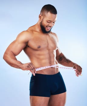 Black man, fitness and body, weightloss and measuring tape with abs, health and active on blue background. Shirtless male bodybuilder, smile and exercise with diet, healthy and strong in underwear