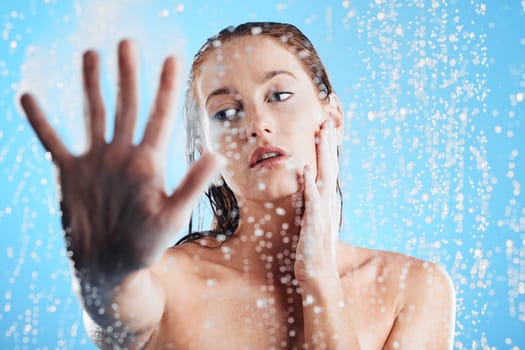 Shower, water drops and woman hand doing skin cleaning, wellness and beauty routine in bathroom. Isolated, blue background and studio with a young female doing hair care and dermatology facial