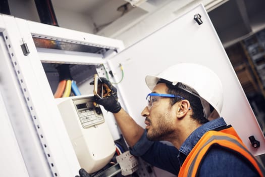 Man, phone and technician in electric inspection for power or sustainable energy at work site. Male electrician, contractor or engineer with smartphone looking to inspect electricity on circuit board