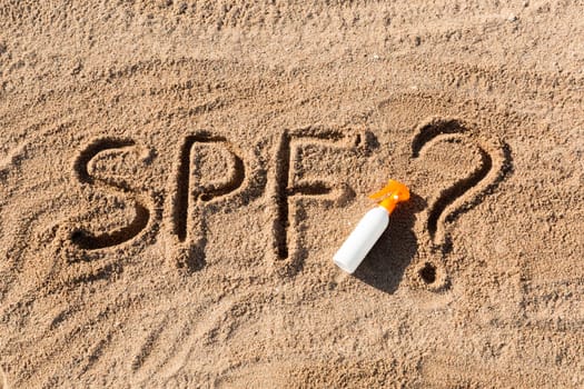 Sun protect factor. SPF word written on the sand and white bottle with suntan cream with question mark. Skin care concept background
