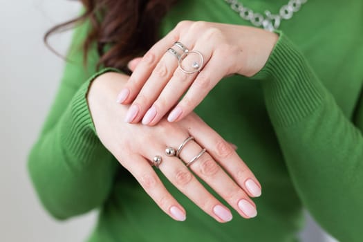 Close up female hands with trendy light pink manicure wear stylish rings jewelry. Silver ring and accessory bijouterie concept