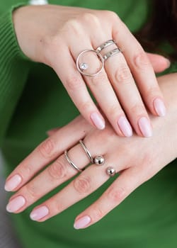 Close up female hands with trendy light pink manicure wear stylish rings jewelry. Silver ring and accessory bijouterie concept