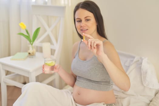 Young pregnant woman taking vitamins. A, D, E, omega-3 capsules