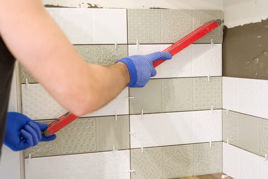 Male worker glues tiles on kitchen wall, uses level and professional materials and tools