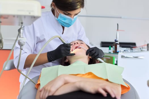 Woman doctor dentist treating teeth to girl patient in dental office. Dentistry, healthy teeth, medicine and healthcare concept