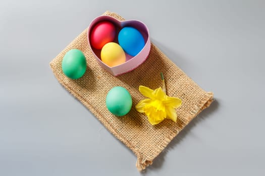 Colored Easter eggs and daffodil flower on sackcloth bag.