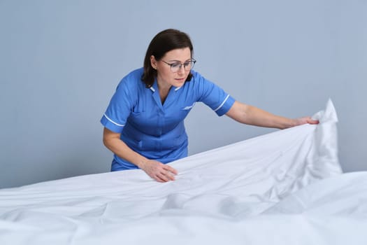Chambermaid making guest bed in hotel bedroom