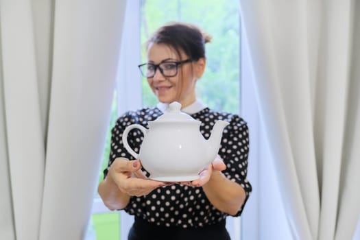 Adult woman holding white porcelain teapot in hands