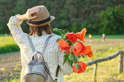 Mature beautiful woman walking along country road with bouquet of poppies