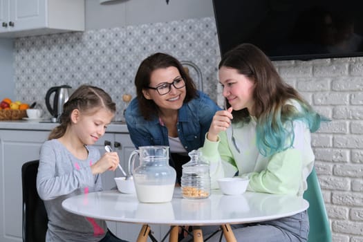 Happy mother caring for daughters in kitchen, eating girls sitting at table