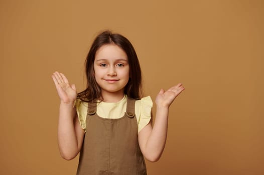 Elementary age child, a lovely girl, smiling cutely at camera, holding her hands palms up on isolated beige background
