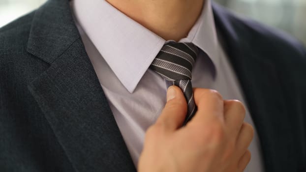 Elegant businessman in suit straightening tie on shirt closeup