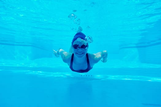 Young girl swimming underwater in the pool, female looking and smiling