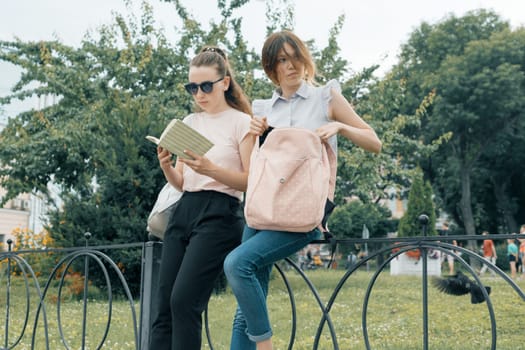 Two learning girls students with backpacks and textbooks outdoor in a park