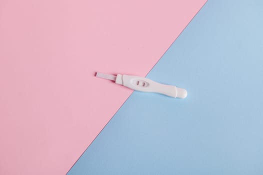 Isolated flat shot of a positive pregnancy test kit on a pink and blue pastel bicolor background. Motherhood concept