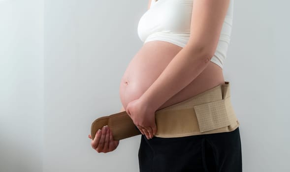 Pregnant woman putting on supporting bandage to reduce backache. Orthopedic abdominal support belt