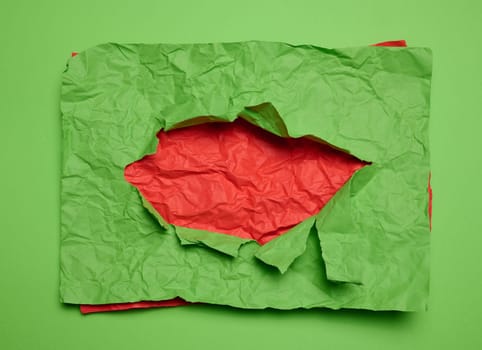 Texture of crumpled green paper with torn hole and red background