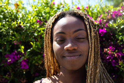 Headshot of african american young woman with eyes closed surrounded by greenery and flowers.