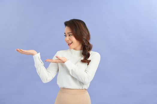 young girl holding copyspace imaginary on the palm to insert an ad on purple background