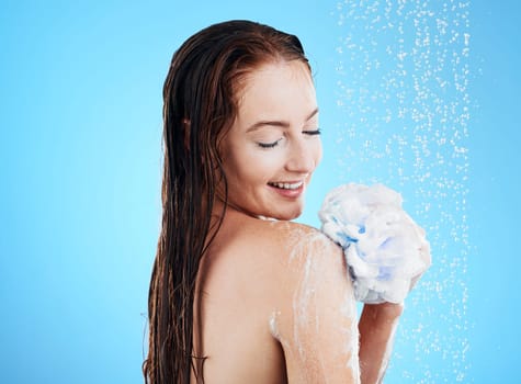Woman in shower, happy with loofah and soap, hygiene and water drops with skincare on blue background. Washing, grooming and cosmetic care with female cleaning body, foam and mockup space in studio
