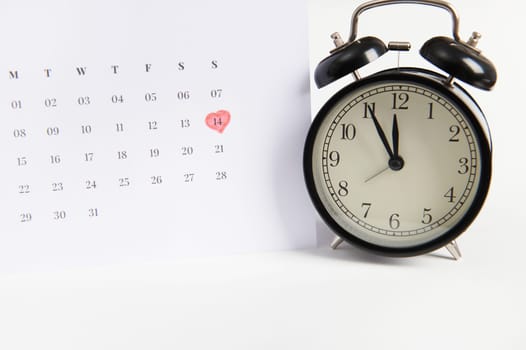 Still life with black alarm clock and a calendar marked with a red marker on the 14th of February. Saint Valentine's Day