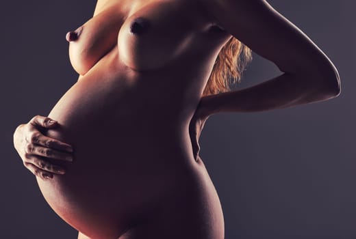 Pregnancy, naked woman in studio with hand on stomach and aesthetic dark background at maternity reveal. Creative photoshoot, art and nude pregnant mother holding belly with healthy body and wellness