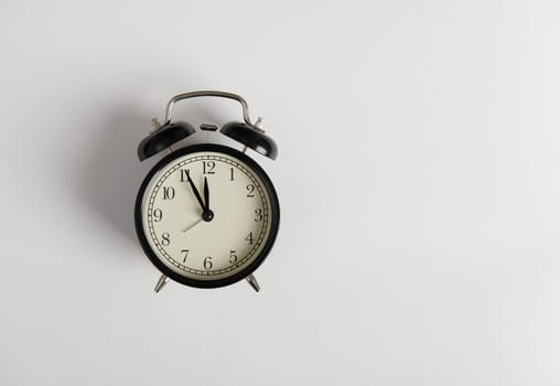 Still life black alarm clock showing 5 minutes to midnight on clock face, isolated over white background with copy space