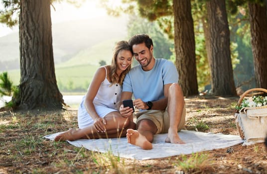 Couple on picnic, phone and relax together in nature, happy people with social media, travel with bonding outdoor. Happiness, man and woman, communication with trust and love in relationship.