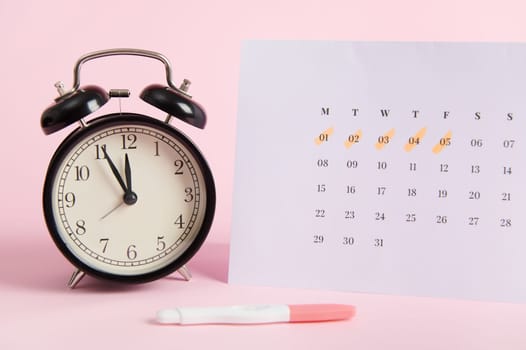 Still life: alarm clock, calendar and pregnancy test on pinp background. Fertility Ovulation Maternity planning concept