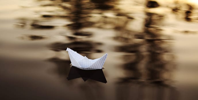A paper boat is floating on the waves in the water at a beautiful sunset. Origami ship Sailing. The concept of a dream, future, childhood, freedom or hope.
