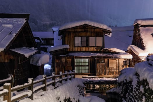 Heavy snow falls on traditional wooden homes in Japanese village at night