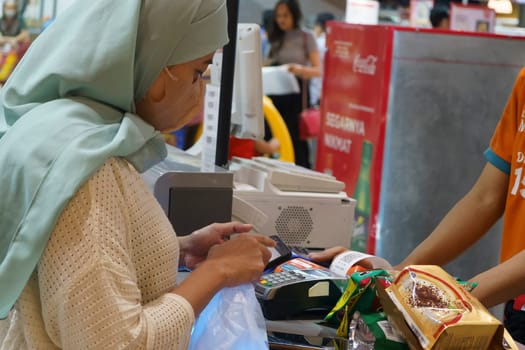 March 25, 2023. Muslim woman paying her shopping with her smartphone in grocery store in Surabaya, Indonesia.