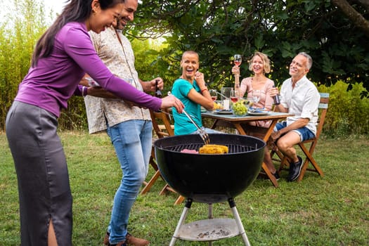 Friends cooking food on grill. Outdoor garden barbecue party. Friends laughing and having fun, enjoying wine in backyard