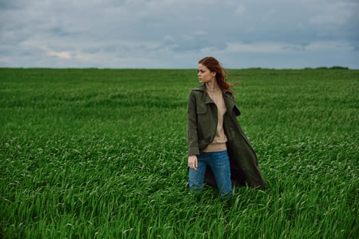 a woman in a coat stands in the middle of a field in cloudy weather in a strong wind turned sideways to the camera. High quality photo