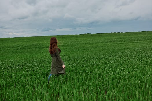 a woman in a long raincoat stands with her back to the camera, far away in a field in rainy, cloudy weather. High quality photo