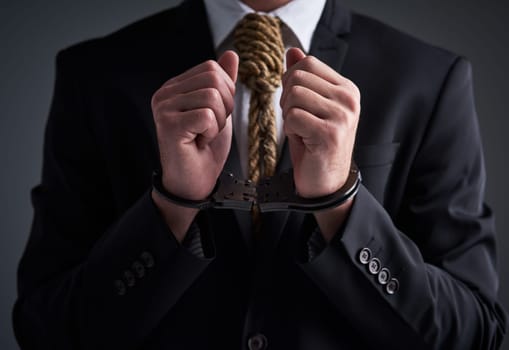 Crime doesnt pay. Studio shot of a handcuffed businessman with a noose tied around his neck for a tie against a gray background.