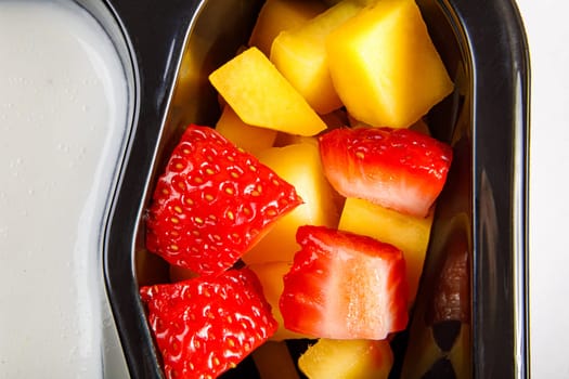 Portion of yogurt dessert with strawberry and mango in a plastic cup. Close-up.