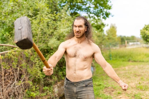 Strong country man with bare torso and a hammer