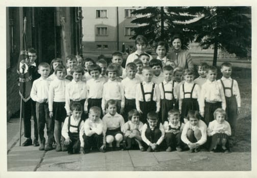 THE CZECHOSLOVAK SOCIALIST REPUBLIC - CIRCA 1960s: Retro photo shows small pupils and they female teachers - schoolmistresses pose for photograper outside. Vintage black and white photography.