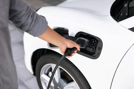 Closeup focus hand insert EV charger to progressive electric rechargeable car.