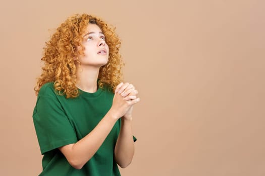 Woman looking up while praying with folded hands