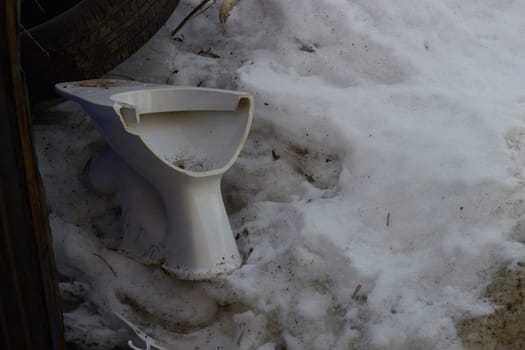 broken white toilet bowl a background dirty snow.